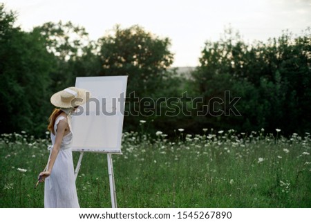 young woman outdoors an easel with a white canvas draws