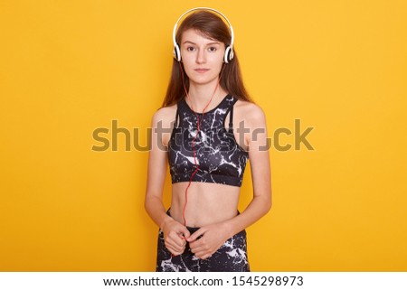 Picture of attractive fitness girl wearing sportwear posing isolated over yellow background, ready for working out in gym, lady has dark staright hair, looks at camera. Fashion and livestyle concept.
