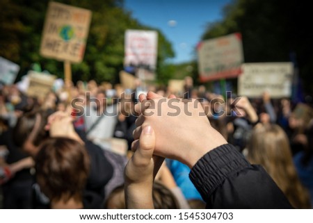 two young people at a rally, joining hands together signaling peace, unity and decisiveness in front of a crowd carrying protest placards with shallow depth of field