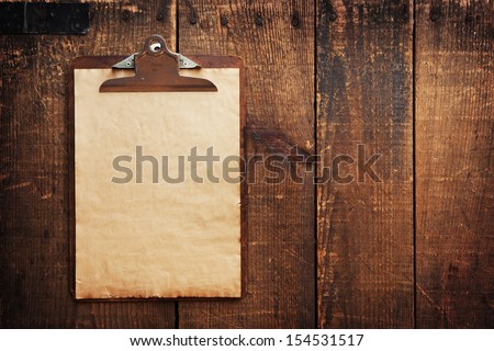 Old clipboard on grungy wooden surface, with plenty of copy space. Royalty-Free Stock Photo #154531517