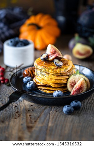 Pumpkin pancakes with syrup or honey, flax seeds, figs, blueberries in a dark plate on the table, selective focus, copy space for your text