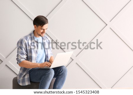 Handsome man with laptop near light wall