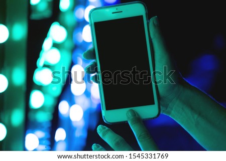 Woman's hand showing smartphone screen in neon blue and pink lights