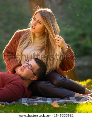 Young man relaxing with his wife in a park in warm evening light lying on the grass with his head in her lap sleeping