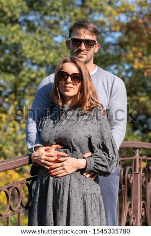 Loving young couple posing on a wrought iron bridge outdoors in an autumn park standing in a close embrace smiling at the camera