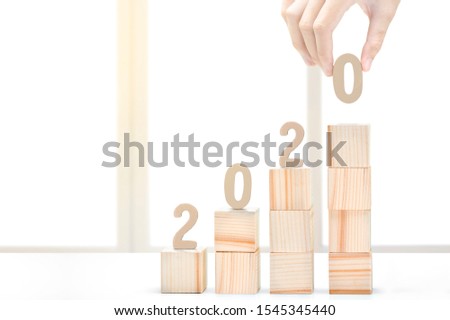 Hand put the number 0 to make 2020 on stairs of wooden block toy on the desk. Happy New Year 2020