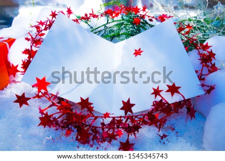 An open Christmas Card on a bed of snow, red star-glitter and green juniper.