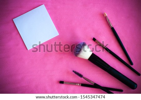 Cosmetic accessories, makeup brushes with empty paper note with copy space on a pink background. Empty note card with makeup products. Sticker for writing a message. Put your job. 