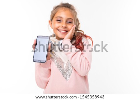 touched little beautiful girl holding a phone in front of her hands and looking at the camera, put her palm to her face against the background of the orange wall