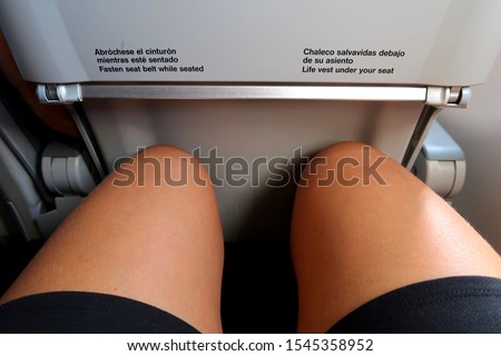 Tight airplane seat with very little legroom, female legs and knees squeezed tight on an aircraft, uncomfortable seat                                Royalty-Free Stock Photo #1545358952