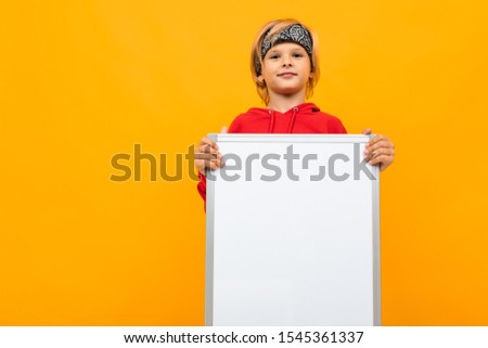 handsome boy in a red hoodie and black bandana on a yellow background with a magnetic board for text with a smile looks at the camera