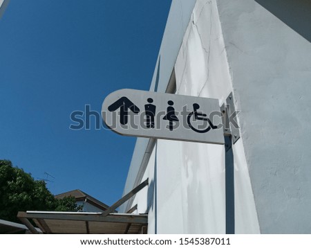 Signs for the bathroom, men, women, and disabled at the corner of the white building. 