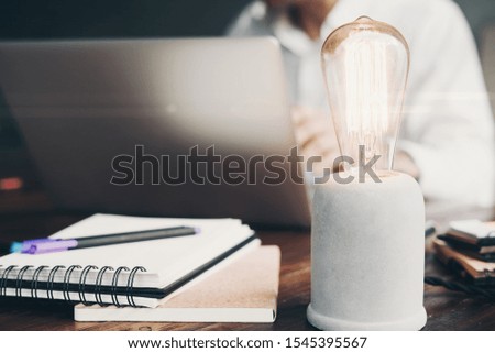 Close up of glowing bulb. Man working on laptop on background. Idea or creativity concept