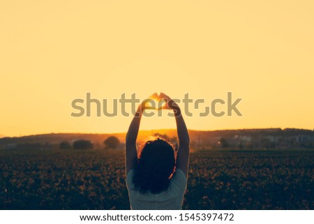 Young woman making heart with her hands at sunset