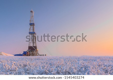 In a winter snow-covered tundra, a well is being drilled at an oil and gas field. Polar day. Beautiful sky. The drilling rig is covered in snow. Royalty-Free Stock Photo #1545403274