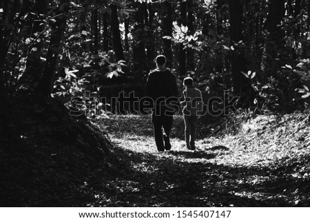 Father and son walking in picturesque autumn forest in French countryside. Back view. Natural lifestyle concept. Family vacation background. Fatherhood concept. Black white photo.