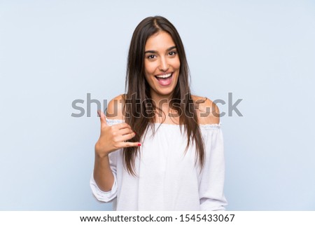 Young woman over isolated blue background making phone gesture