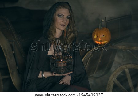 A woman in black mantle - the image of a witch on Halloween in dark vintage interior
