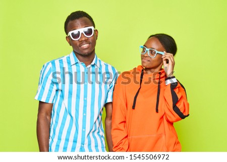 African-Americans in sunglasses on a green background hug each other