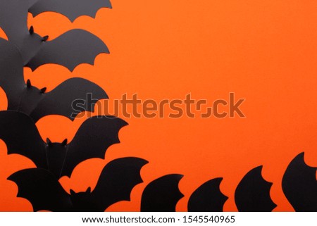 Conceptual halloween flat lay on a bright orange background. Black hand made paper bat as a symbol of halloween parties.