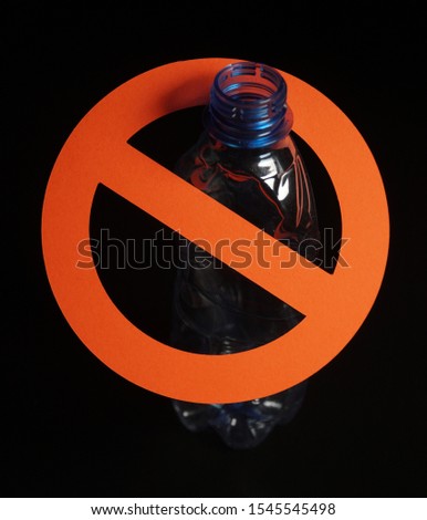 Empty blue plastic bottle in a stop sign on black background. Concept of stop plastic pollution, global warming, recycling plastic, plastic free.
