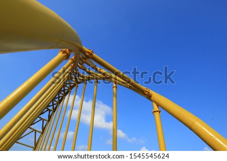 A close-up of abstrack construction of yellow painted round iron in Indramayu "Jembatan Kuning" and behind the sky is blue.