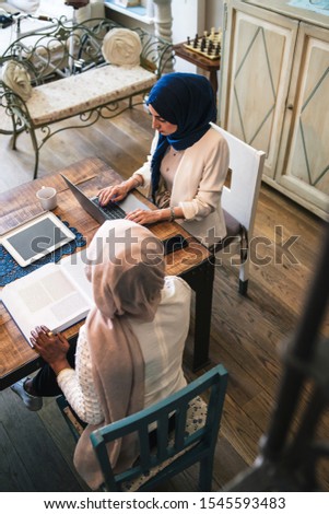 Two young Muslim women study on books and laptop at the kitchen table - Arabian Millennials are preparing for university exams - Top view