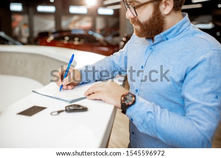 Young man signing some documents, buying or renting a car in the modern showroom of the car dealership