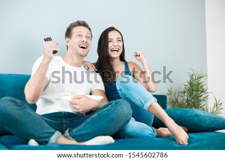 young couple beautiful brunette woman and handsome man cheer on their favorite team while watching football game eating popcorn at home cozy lifestyle