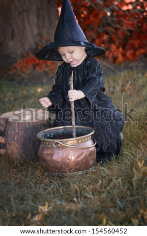 Little halloween witch , boiling a potion, outdoors in the woods