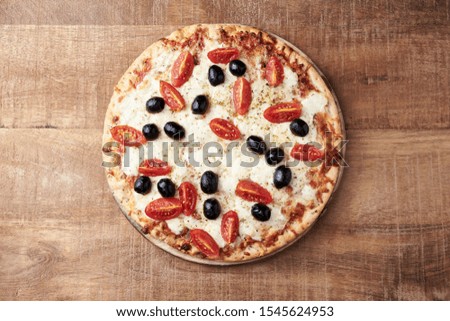 Pizza with mozzarella cheese, cherry tomatoes, black olives and oregano. Home made food. Concept for a tasty and hearty meal. Rustic wooden background. Top view. Copy space. 