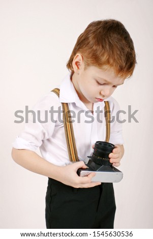 Little boy hold and learn vintage retro film photocamera at studio indoors, stylish small photographer 