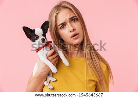 Cute confused lovely girl playing with her pet chihuahua isolated over pink background