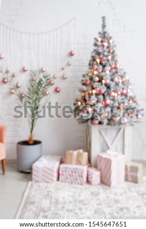 Blurry interior of a light living room with white brick wall a Christmas artificial spruce decorated with lights and balls with gift boxes in wrapping paper. Concept of cozy home christmas decor