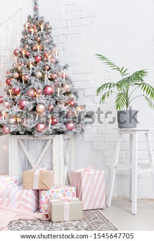 Cozy bright Christmas living room white brick wall decorated with Christmas balls peach armchair standing near an artificial Christmas tree decorated with balls in a wooden box next to gift boxes