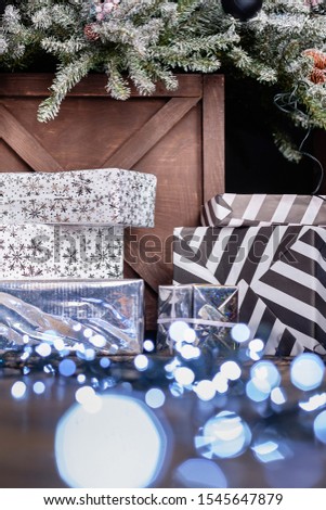 Christmas decor close-up gifts in boxes in gift wrapping lie under an artificial fir tree painted with silver and a toy lying on the floor next to a led garland. Christmas Eve concept