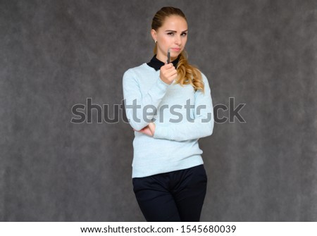 Portrait of a pretty blonde financial secretary girl with long curly hair in a business suit standing in the studio on a gray background with emotions in various poses.