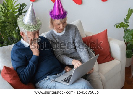 senior elderly caucasian old man and woman playing internet by using laptop together in living room that decorated with christmas tree for christmas festival day, retirement lovely lifestyle concept