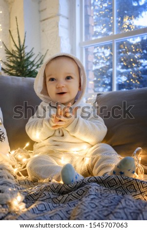 Christmas morning. A child in a white suit sits joyful on the bed. Around him are light bulbs, garlands.