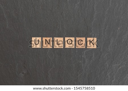 Unlock written with game style wooden letters, on a grey slate background