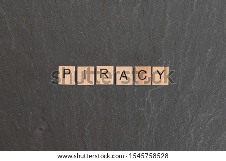 Piracy written with game style wooden letters, on a grey slate background