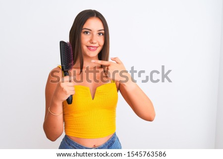 Young beautiful girl holding hair comb standing over isolated white background very happy pointing with hand and finger