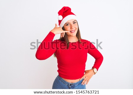 Young beautiful girl wearing Christmas Santa hat standing over isolated white background smiling doing phone gesture with hand and fingers like talking on the telephone. Communicating concepts.