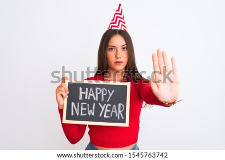 Beautiful girl wearing fanny party hat holding blackboard over isolated white background with open hand doing stop sign with serious and confident expression, defense gesture
