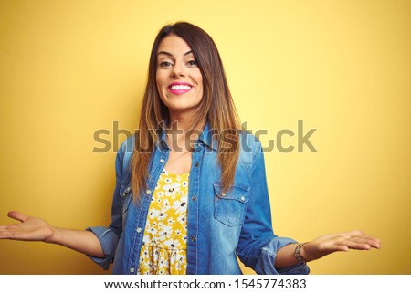 Young beautiful woman standing over yellow isolated background smiling cheerful with open arms as friendly welcome, positive and confident greetings