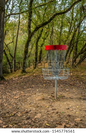 In the woods on the course trails is a empty disc golf basket #5 with trees in the background on a sunny day in autumn
