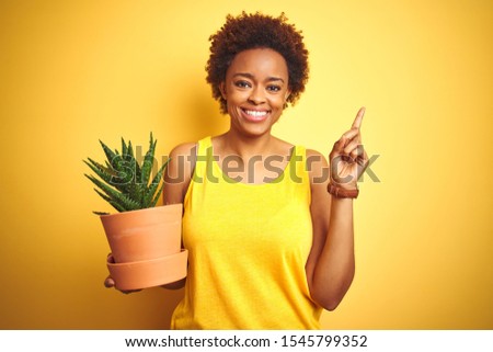 Young african american woman holding cactus pot over isolated yellow background very happy pointing with hand and finger to the side