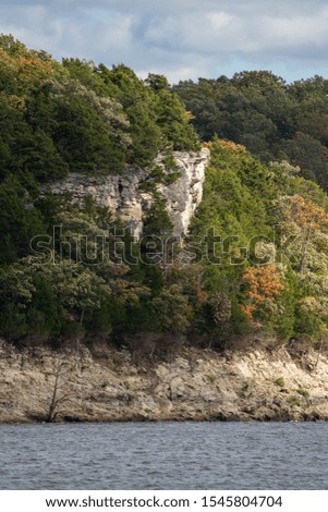 A cliff face among the trees in this fall scene bordering a lake. These banks are a popular fishing spot for boaters to anchor to.