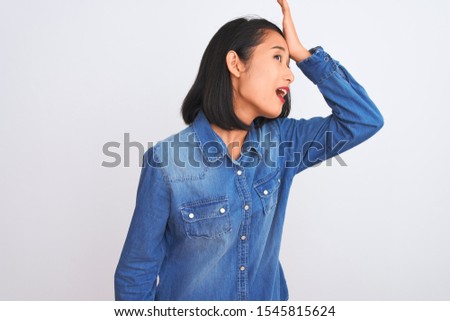 Young beautiful chinese woman wearing denim shirt standing over isolated white background surprised with hand on head for mistake, remember error. Forgot, bad memory concept.