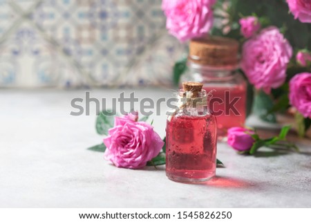Natural pure rose oil or scented water in bottles for spa, skin care or aromatherapy. Glass bottle on a wooden table, small pink roses with leaves. Organic cosmetics concept. Selective focus